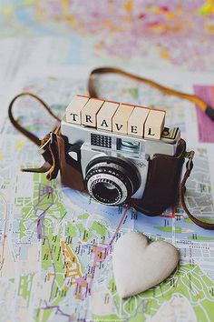 an old camera sitting on top of a map next to a small white heart shaped object