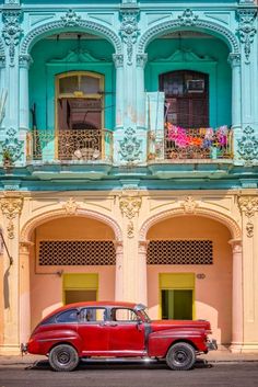 an old red car is parked in front of a pink and blue building with balconies