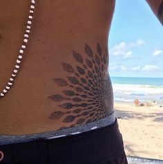 a woman's stomach with a flower tattoo on the side and an ocean in the background