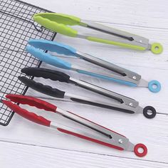 five different colored kitchen utensils sitting on a wire rack next to each other