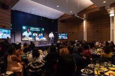 a group of people sitting at tables in front of large screens with food on them