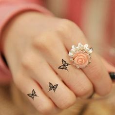 a woman's hand with three small tattoos on her fingers and an orange rose in the middle