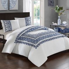 a bed with white and blue comforters in a bedroom next to a table on hardwood floors