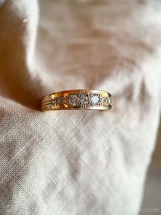 a gold wedding band with three diamonds on the top and bottom, sitting on a white cloth