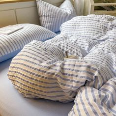 an unmade bed with blue and white striped pillows