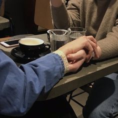 two people sitting at a table holding hands over a coffee cup with their fingers on each other's hand