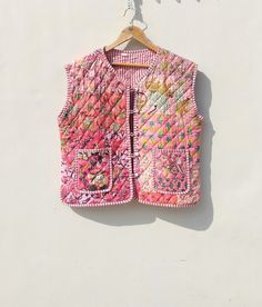 a pink vest hanging from a clothes line on a white wall next to a wooden hanger