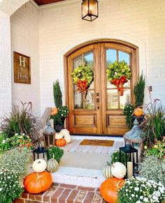 the front door is decorated with pumpkins and greenery for fall time, while two lanterns are on either side of the entryway