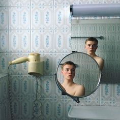 a young man is reflected in the mirror of a bathroom with blue and white wallpaper