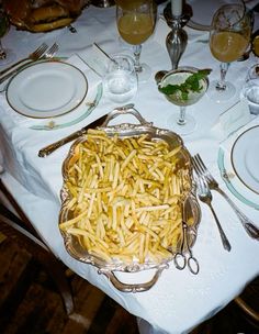 a large platter of french fries sits on a table with silverware and wine glasses