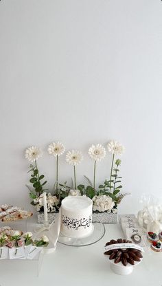 a white cake sitting on top of a table next to other cakes and flowers in vases