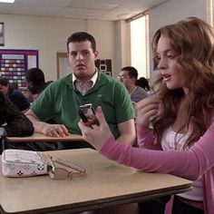 two people sitting at a table with cell phones in their hands and one person standing next to the table