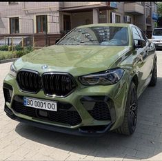 a green bmw suv parked in front of a building on a brick street with other cars behind it