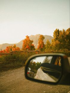 a car's side view mirror is shown as it drives down a dirt road