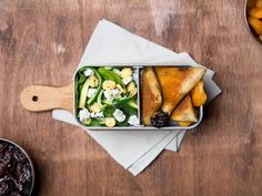 a bento box filled with food sitting on top of a wooden table next to bowls of fruit and raisins