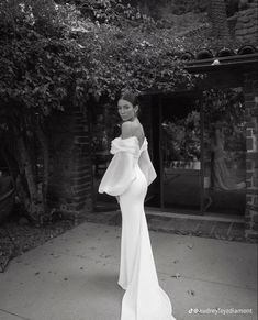 a woman in a white dress standing on the sidewalk with her hands behind her back