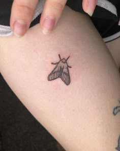 a small black and white moth tattoo on the right thigh, next to a woman's leg