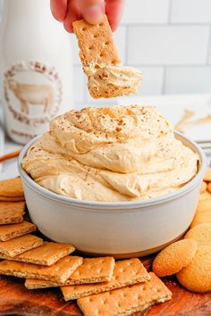 a person dipping some crackers into a bowl of humongous dip surrounded by crackers