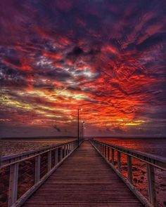 a wooden pier with the sun going down over water and clouds in the sky above it