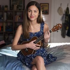 a woman sitting on a bed playing an ukulele