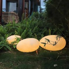 three lights that are sitting in the grass next to some plants and bushes, with one light turned on