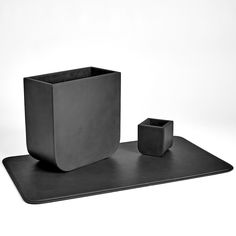 a black square vase sitting on top of a table next to a cup and saucer