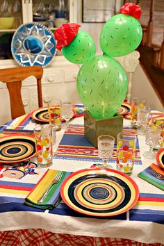 a table topped with plates and glasses filled with colorful balloons in the shape of mickey mouse heads