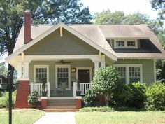 a gray house with white trim on the front door and porch is surrounded by greenery