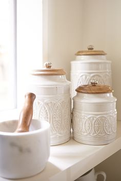 three white canisters sitting on top of a shelf next to a bowl and spoon