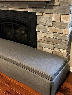 a gray bench sitting in front of a fire place with a stone fireplace behind it