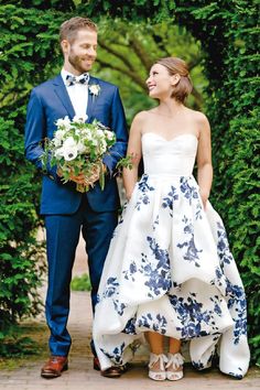 a man and woman standing next to each other in front of some green bushes holding hands