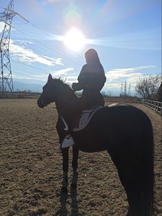 a woman riding on the back of a brown horse in an open field next to power lines