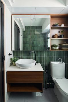 a bathroom with green tiled walls and a white toilet next to a wooden sink vanity