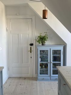 an empty kitchen with white walls and wooden flooring next to a blue cabinet filled with drinks