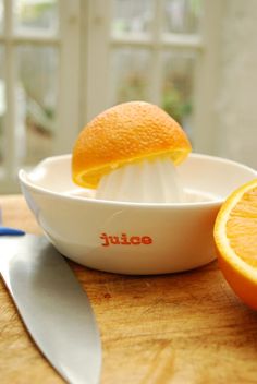 an orange being squeezed into a bowl with a knife on the table next to it