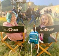 two women sitting in lawn chairs with black widow signs on their backs, smiling at the camera