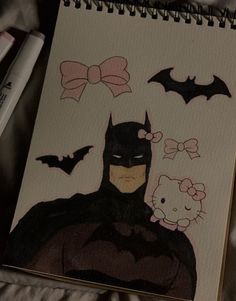 a drawing of batman and hello kitty on a sheet of paper with marker pens next to it