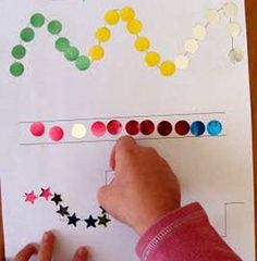 a child's hand writing on a piece of paper with colored circles and stars