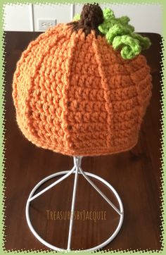 an orange crocheted pumpkin sitting on top of a white wire stand with green leaves