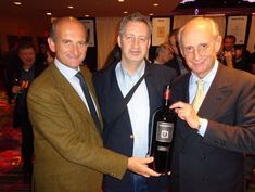 three men standing next to each other holding a wine bottle