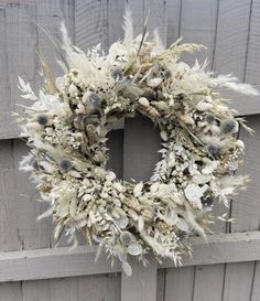 a wreath is hanging on the side of a wooden fence with white flowers and feathers