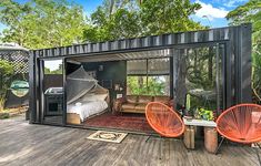 a tiny house made out of shipping containers is on the deck with two orange chairs