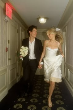 a man and woman walking down a hallway holding hands