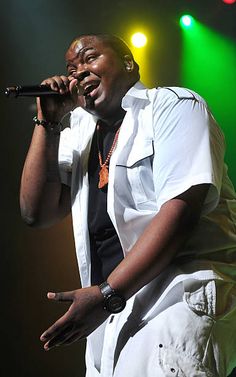 a man in white shirt singing into a microphone on stage with green and red lights behind him