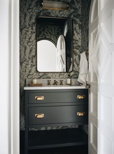 a bathroom sink with a mirror above it next to a wallpapered wall and door