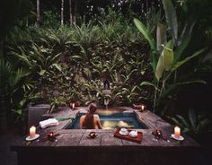 a woman sitting in a hot tub surrounded by greenery and lit candles on the table