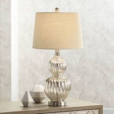 a table lamp sitting on top of a wooden dresser next to a white vase with a beige shade