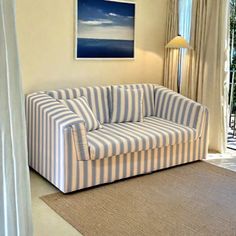 a striped couch sitting in front of a window next to a lamp on a rug