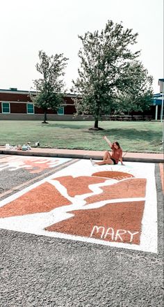 a woman sitting on the ground in front of a sign that says mary and is painted with white paint