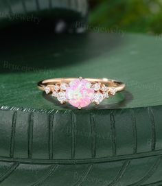 a pink opal and diamond ring sitting on top of a green surface